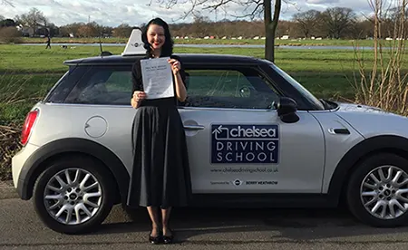 Student holding driving test pass certificate beside Chelsea Driving School car